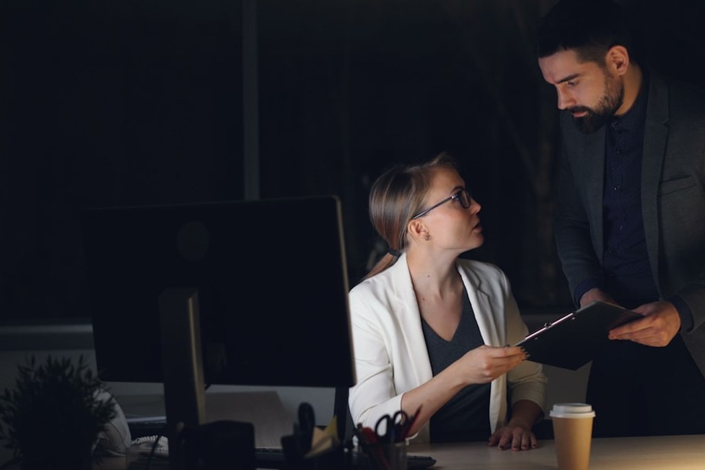 Two colleagues collaborating late in a dimly lit office, coaching high-performer success