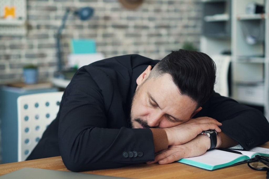 Exhausted male leader resting his head on a desk, overwhelmed by burnout